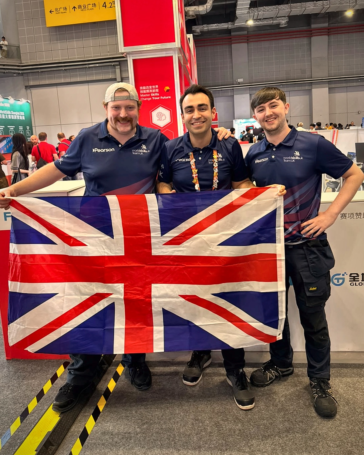 Patrick Sheerin and Caolan McCartan with Omid Teimoori holding the Union flag at WorldSkills Shanghai 2026